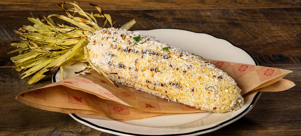 Elote-style grilled corn with cheese and herbs on a rustic wooden surface.