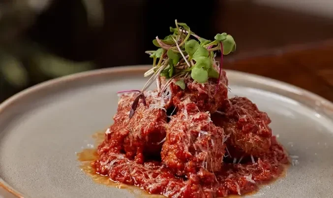 Plate of meatballs in red sauce, topped with Parmesan and microgreens.