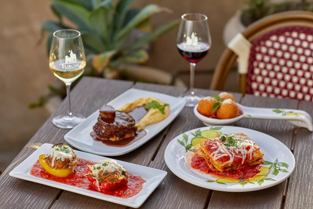 Four gourmet dishes and two wines on a rustic outdoor table.