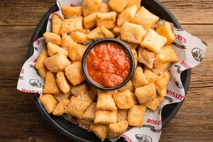 Golden, seasoned garlic knots with red marinara sauce in a black bowl.