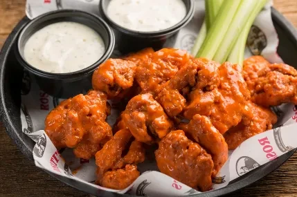 Orange buffalo chicken wings with celery and white dipping sauces.