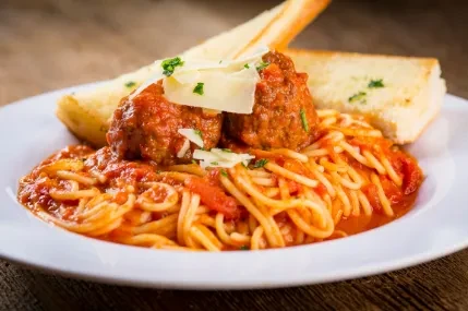 Close-up of spaghetti and meatballs with garlic bread, cheese, and herbs.