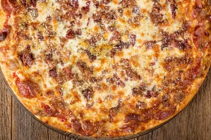 Cooked pizza with melted cheese, meat, and herbs on wood.
