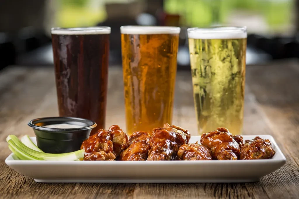 Plate of reddish-brown wings, celery, dip, and three varied beers.