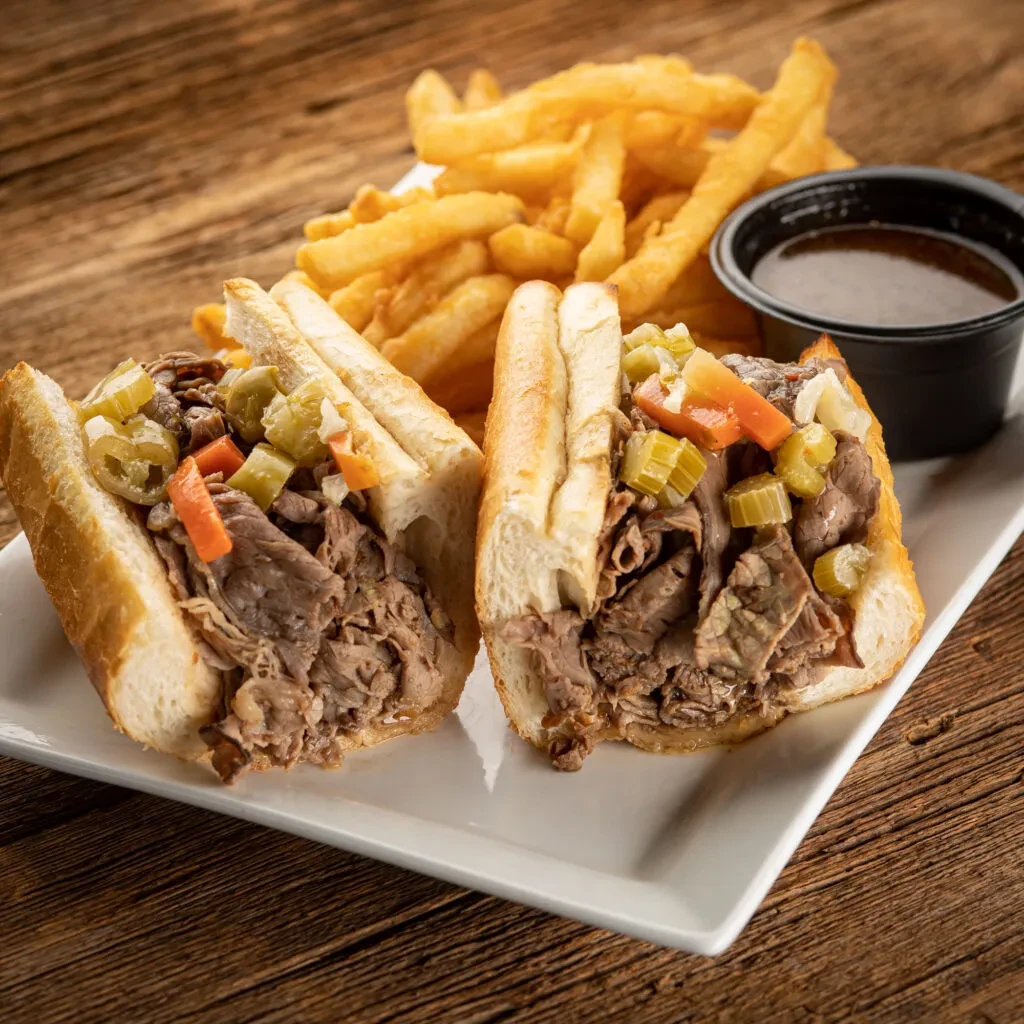French dip sandwich with relish, fries, and au jus on wooden table.