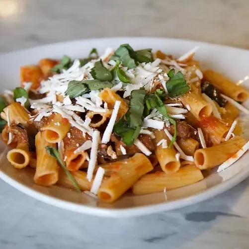 Plate of rigatoni pasta with red ragu, grated cheese, and fresh basil.
