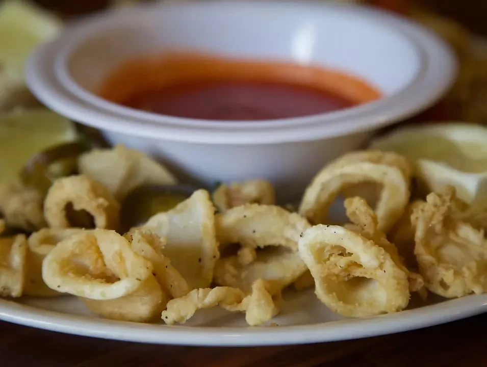 Plate of crispy golden-brown fried calamari with dipping sauce and citrus wedges.