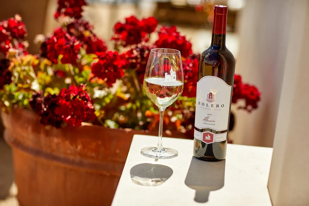 White wine bottle, Bolero Albariño, and glass outdoors with red flowers.