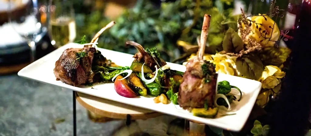 Three bone-in meat portions, vegetables, fruit slice, elegant setting.