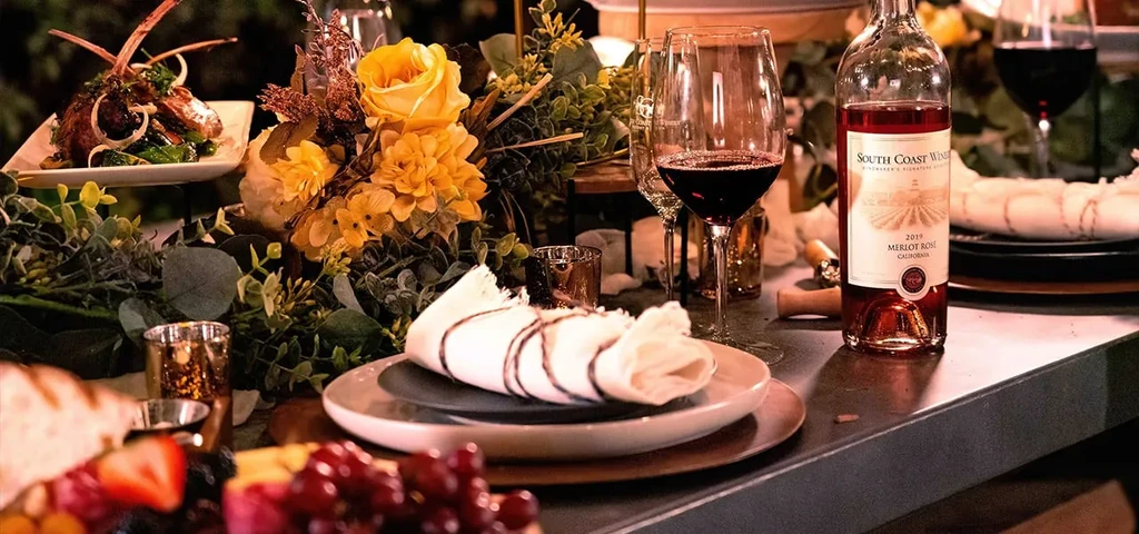 Elegant dining table with wine, lamb, fruit, flowers, and candles.