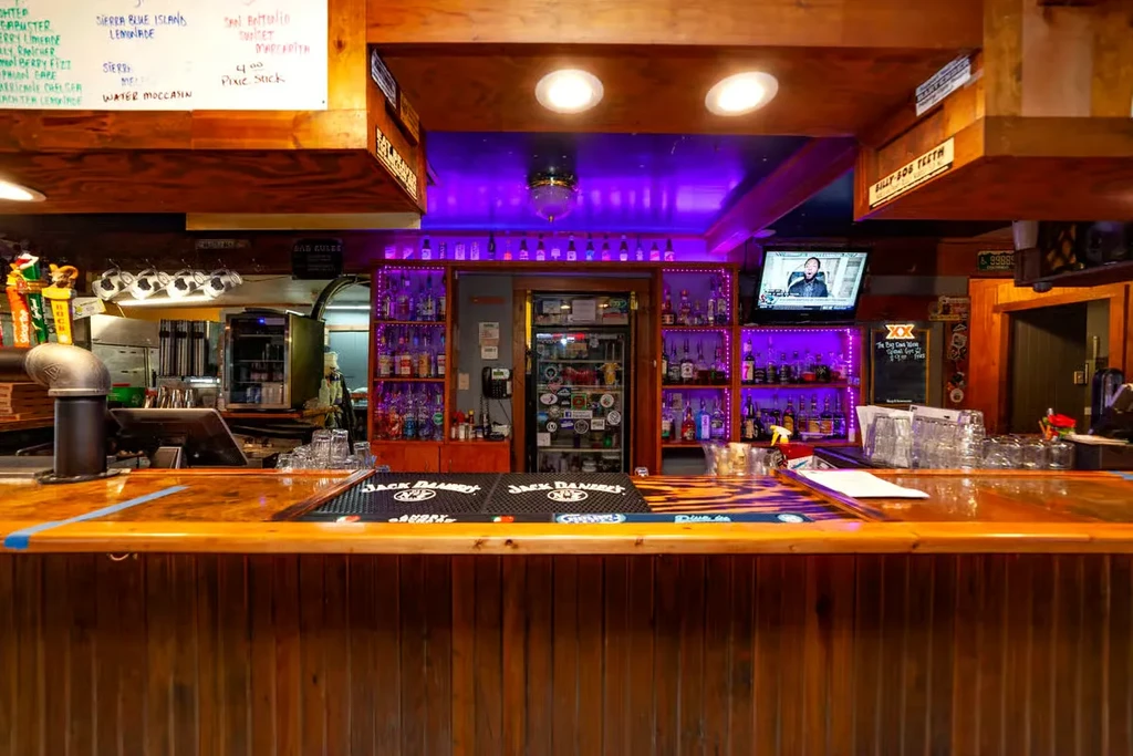 Bar interior: wooden counter, purple-lit liquor shelves, menu, and TV.