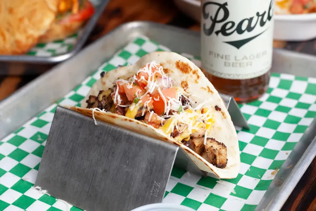 Grilled meat taco with cheese and pico de gallo on a metal holder.