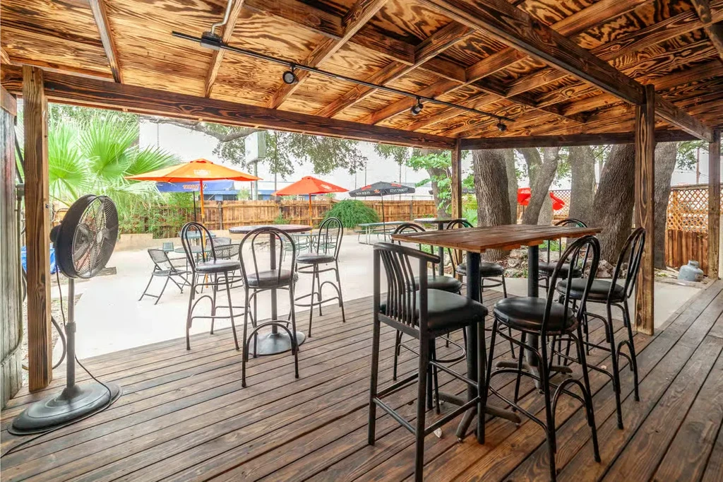 Shaded outdoor restaurant patio with wooden deck, tables, and orange umbrellas.