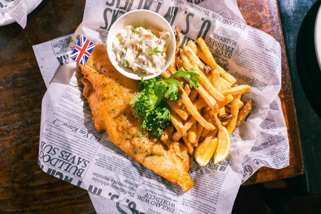 Classic British fish and chips with coleslaw, lemon, and Union Jack flag.