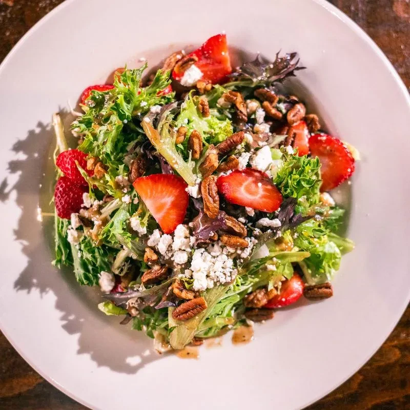 Salad with mixed greens, strawberries, cheese, and pecans in white bowl.