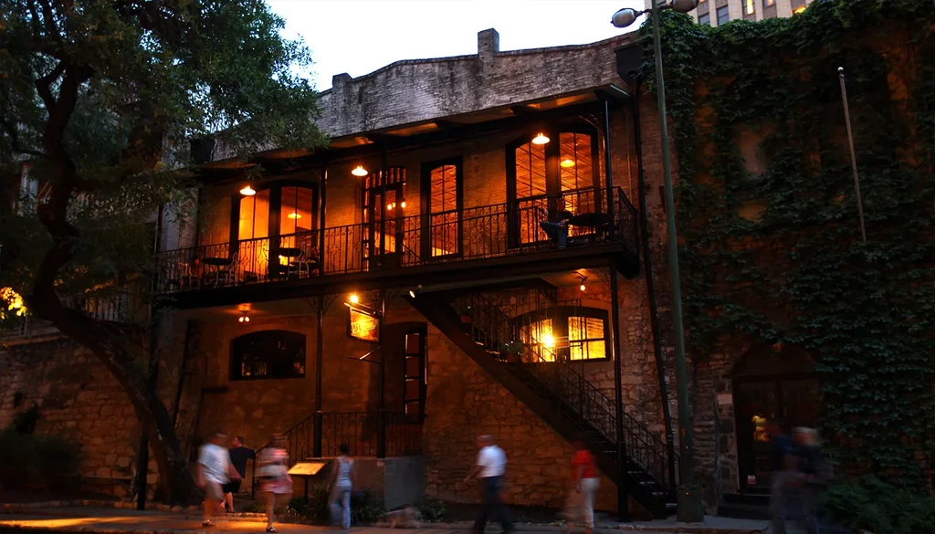 Historic brick building with two lit balconies, a tree, and ivy at night.