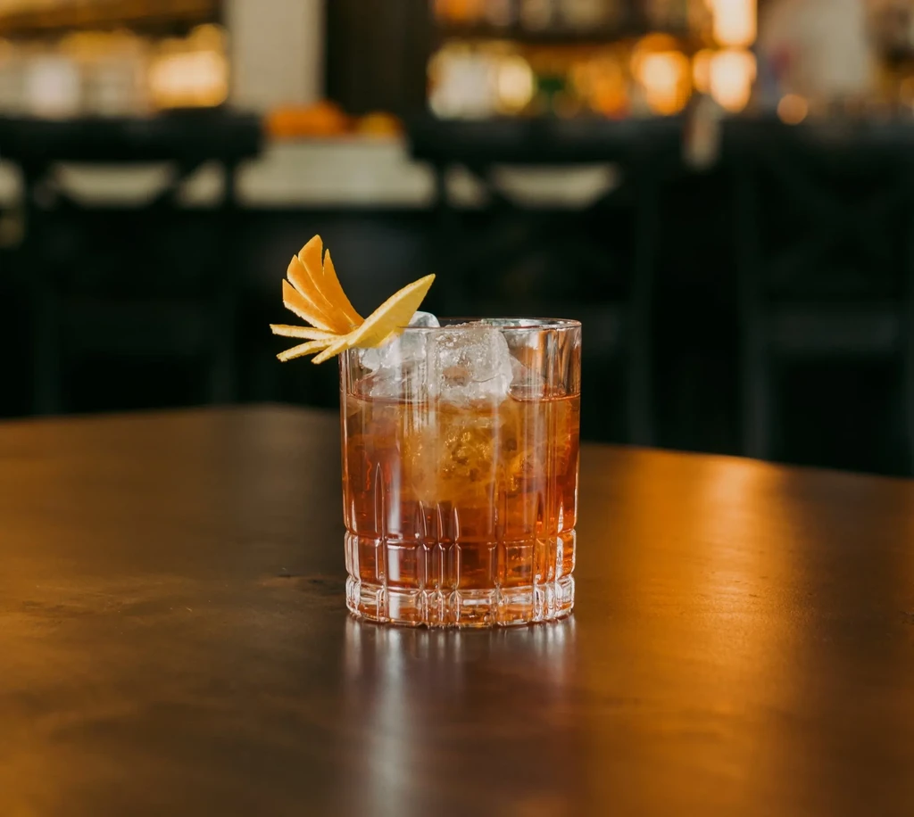 Iced amber cocktail in rocks glass with elaborate orange peel garnish.