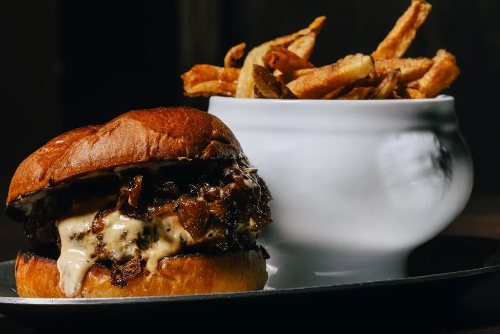 Close-up gourmet burger with melted cheese and hand-cut fries.