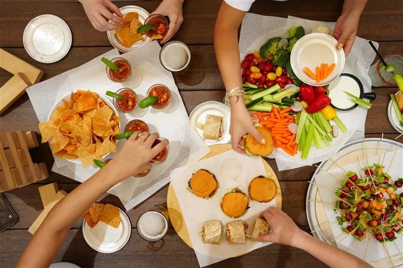Hands share diverse appetizers and drinks on a rustic wooden table.