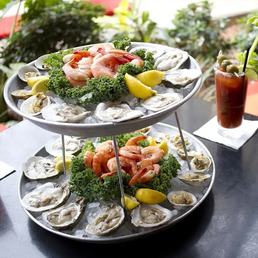 Two-tiered seafood tower with shrimp, oysters, and clams next to a Bloody Mary.