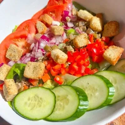 Colorful salad with lettuce, tomatoes, bell peppers, cucumbers, croutons.