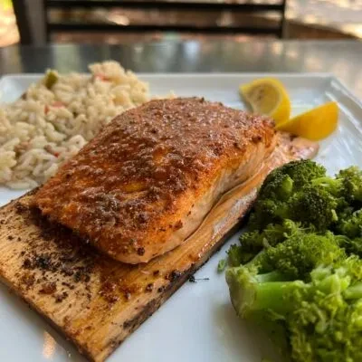 Cedar-planked salmon meal with rice pilaf, broccoli, and lemon wedges.