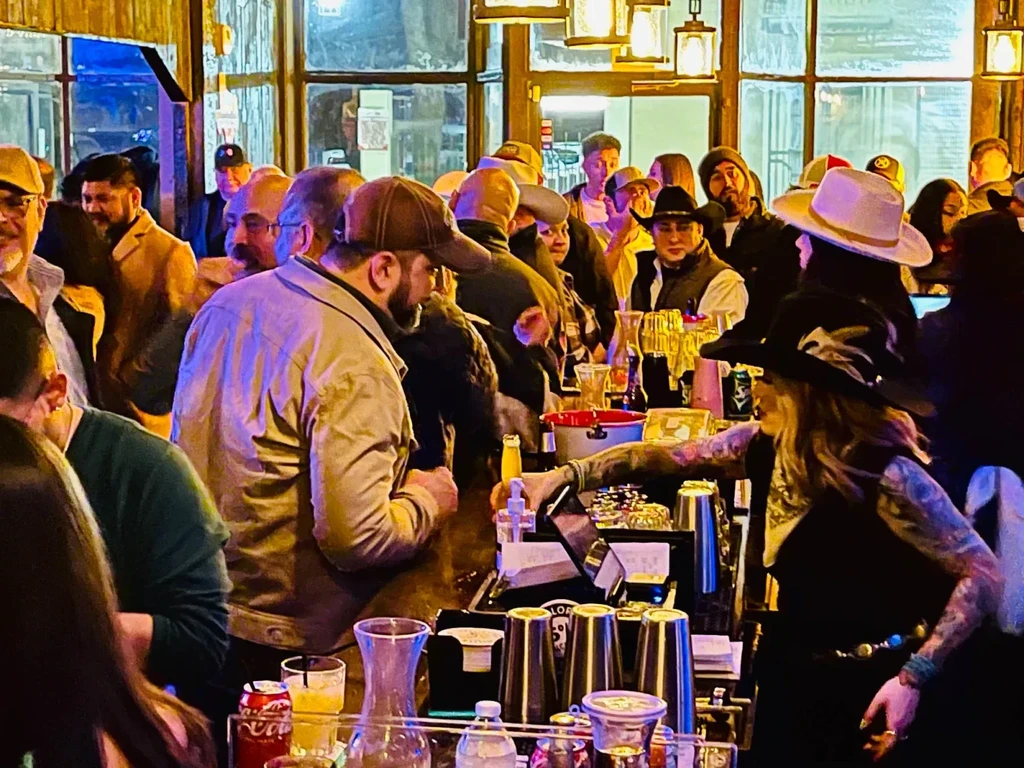 Warm, busy bar scene with a crowd and bartender making drinks.