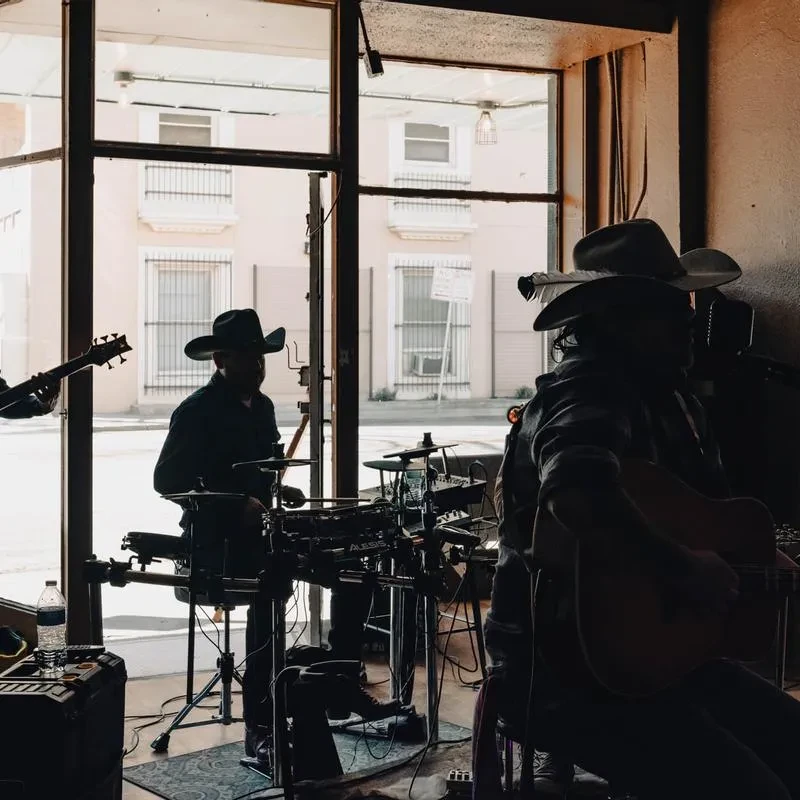 Silhouetted live band performing indoors against bright daytime windows.