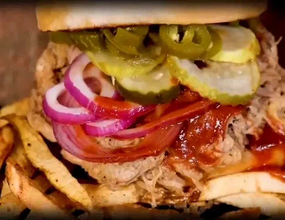 Heavily loaded pulled pork sandwich with onions, pickles, sauce, and fries.