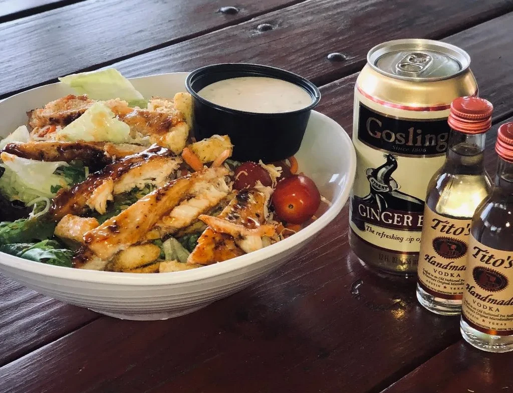 Chicken salad, dressing, ginger beer, and vodka on a wooden table.