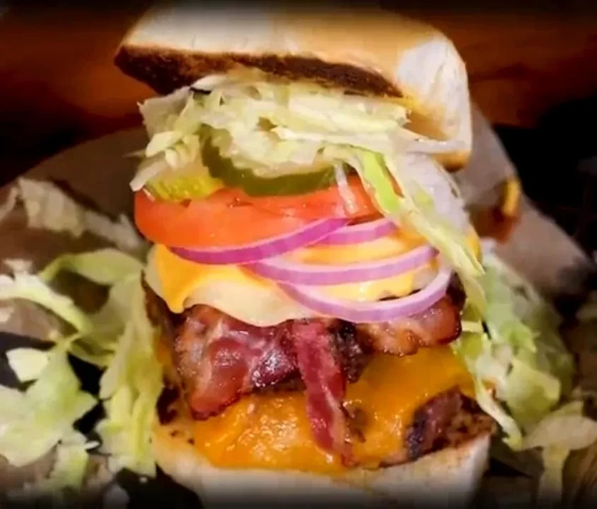 A tall, multi-layered burger with lettuce, tomato, bacon, and cheese.
