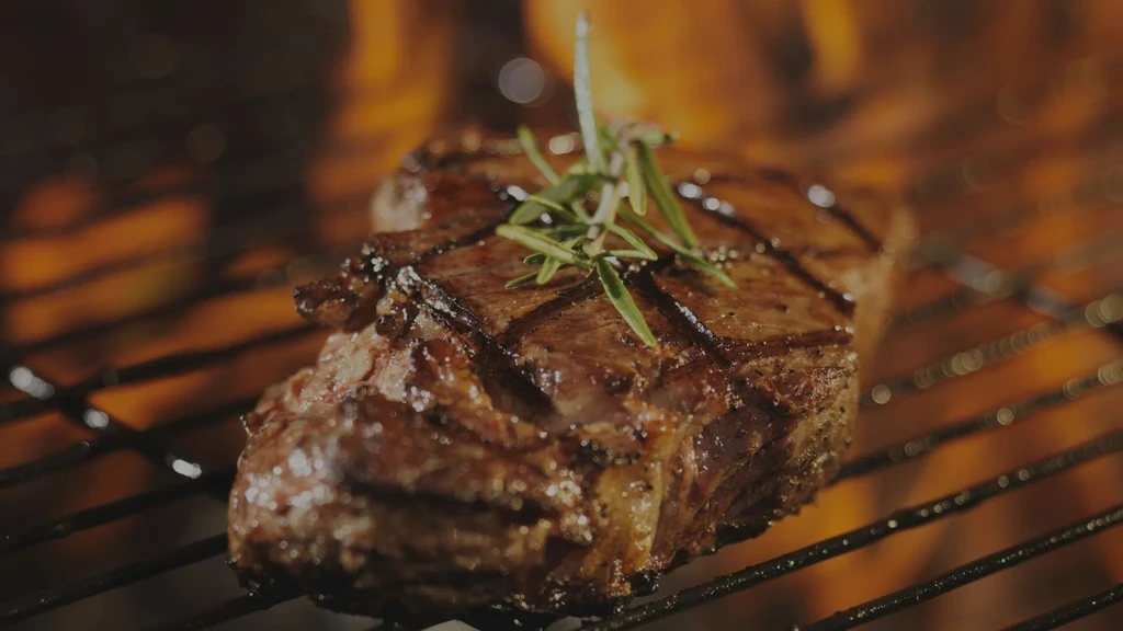 Juicy, thick steak with rosemary grilling, showing dark grill marks.