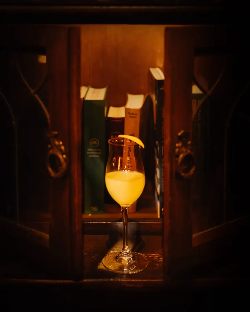 Frothy yellow drink in a stemmed glass with citrus peel.