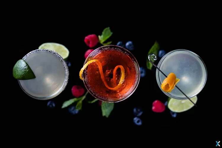 Three colorful cocktails with fresh fruit and mint on a dark surface.