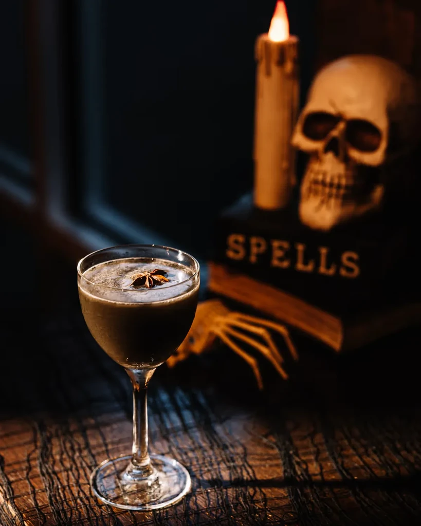 Dark cocktail with star anise, skull, and 'SPELLS' book.