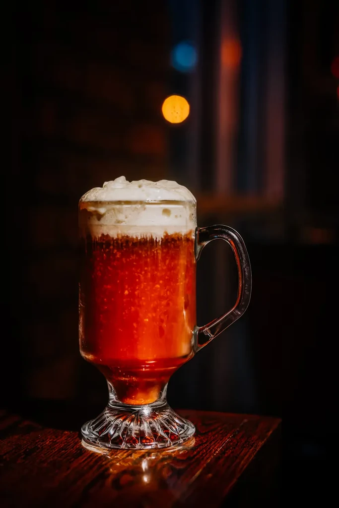 Layered reddish-orange drink with white foam in a clear glass mug.