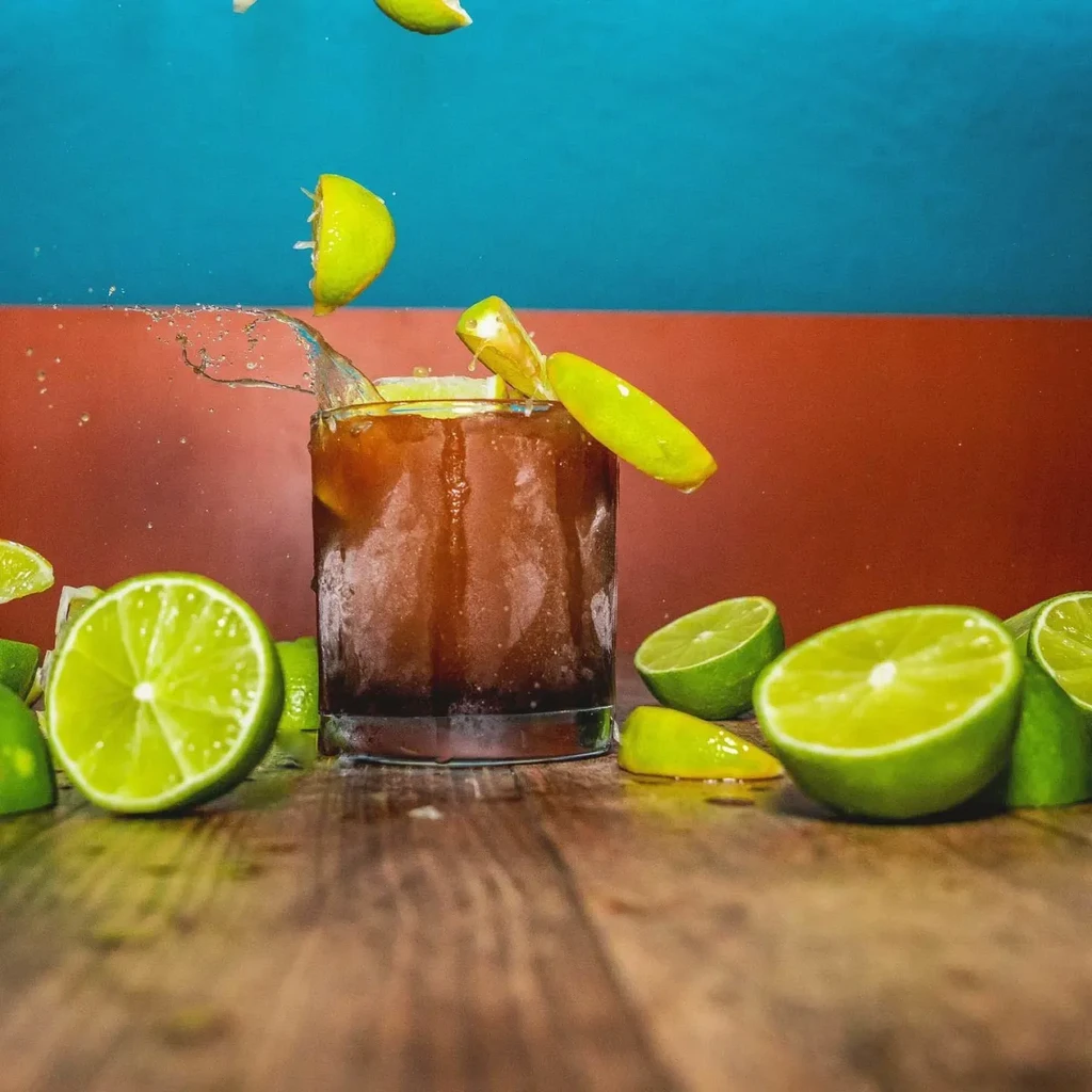 Dark iced drink in frosted glass with limes splashing.