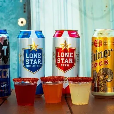 Three chili-rimmed shots and four beer cans on wood.