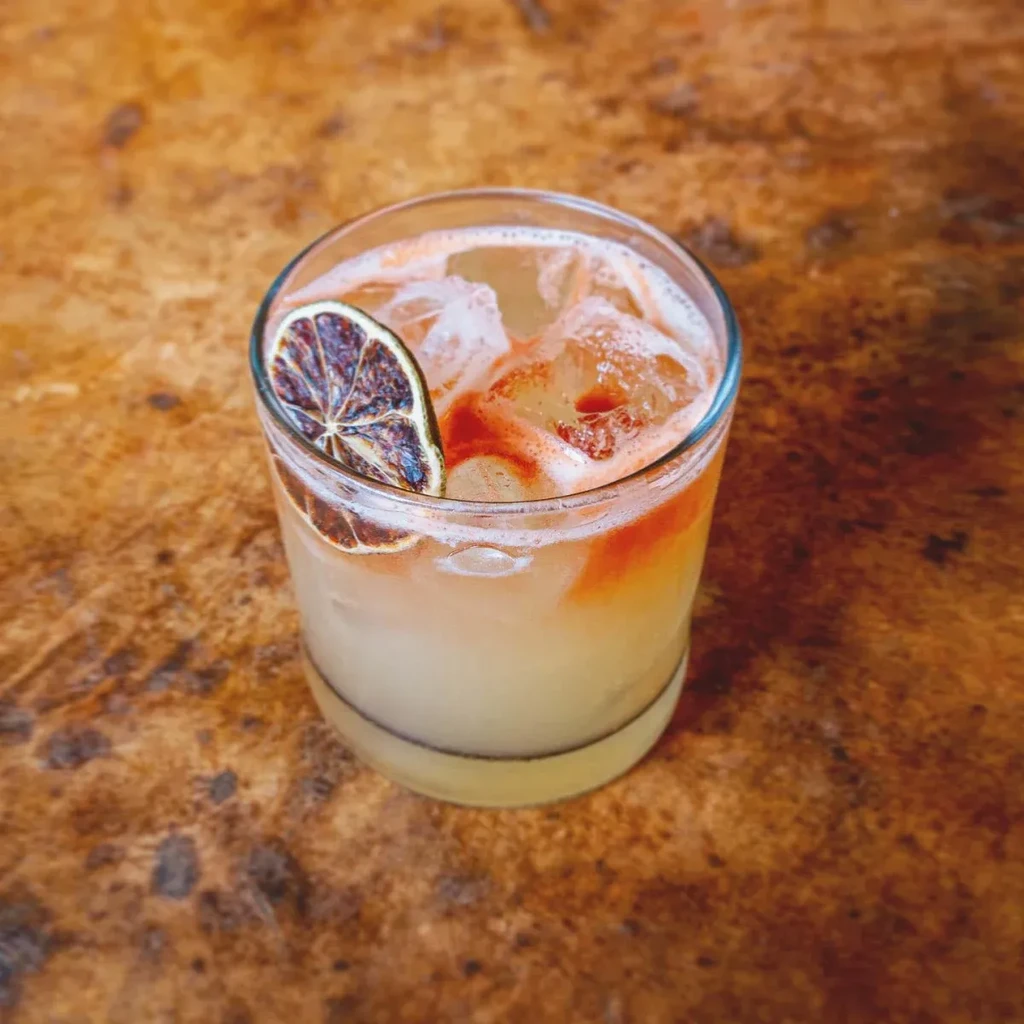 Amber cocktail with ice, reddish swirls, and dried citrus garnish on wood.