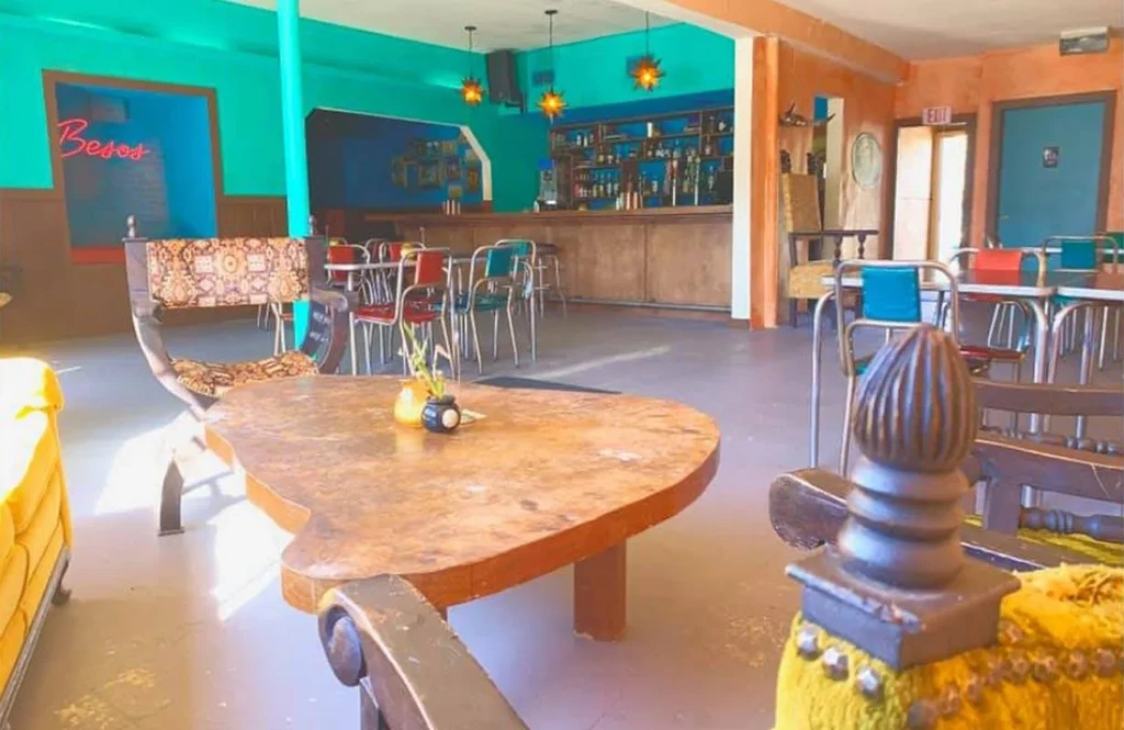 Vibrant, eclectic restaurant bar interior with colorful walls and a neon sign.