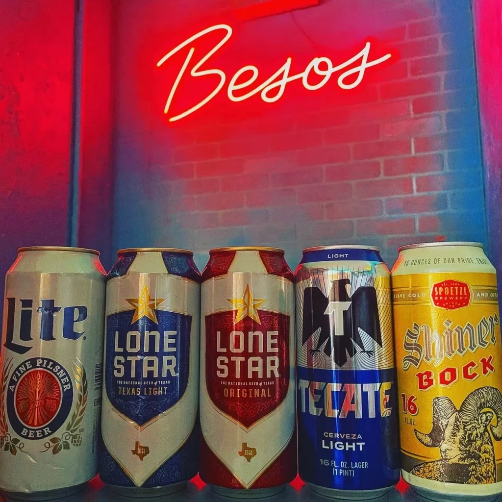 Five beer cans, brick wall, and red 'Besos' neon sign.