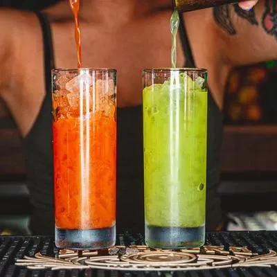 Two layered orange and green iced drinks are being poured.
