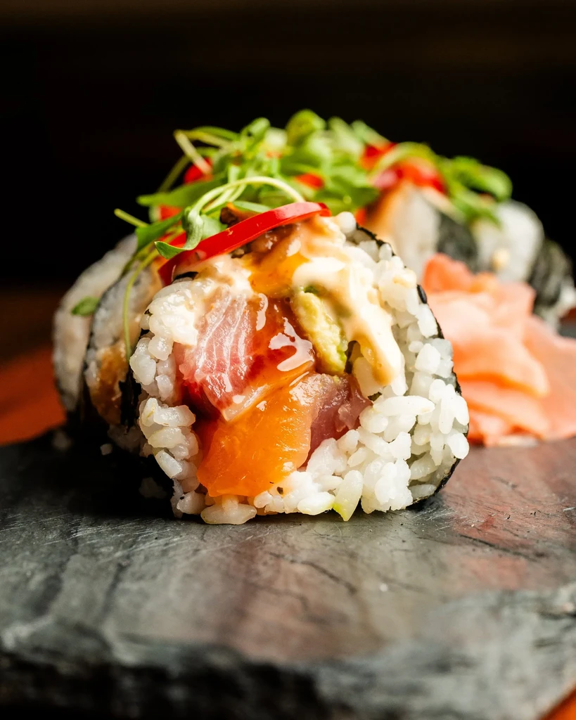 Elaborate sushi roll with tuna, salmon, sauces, and microgreens.