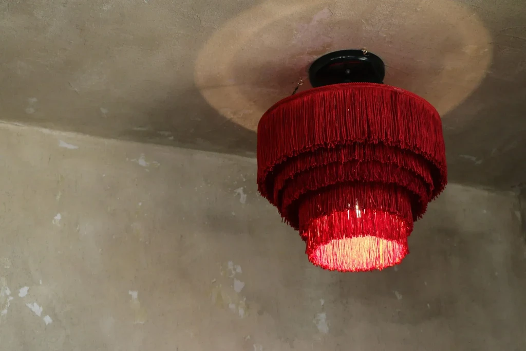 Red fringed chandelier hangs, casting warm glow on textured ceiling.