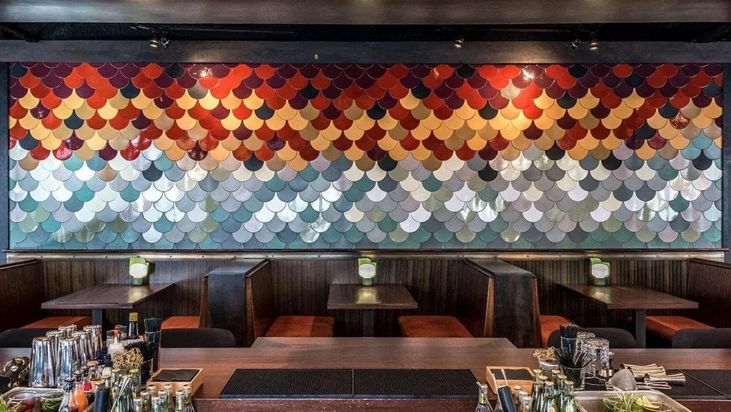 Restaurant interior with a bar, orange booths, and gradient scallop mosaic.