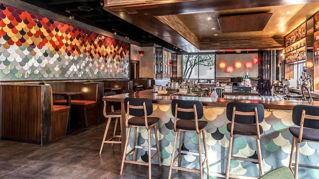 Modern restaurant interior with iridescent mosaic wall and long wooden bar.