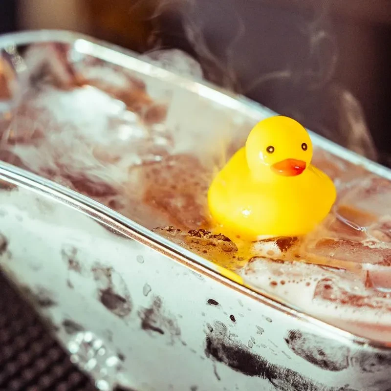 Bright yellow rubber duck floating in a miniature steaming bathtub.