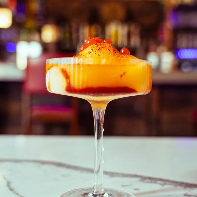 Layered red and orange slushy with berries in a stemmed coupe glass.