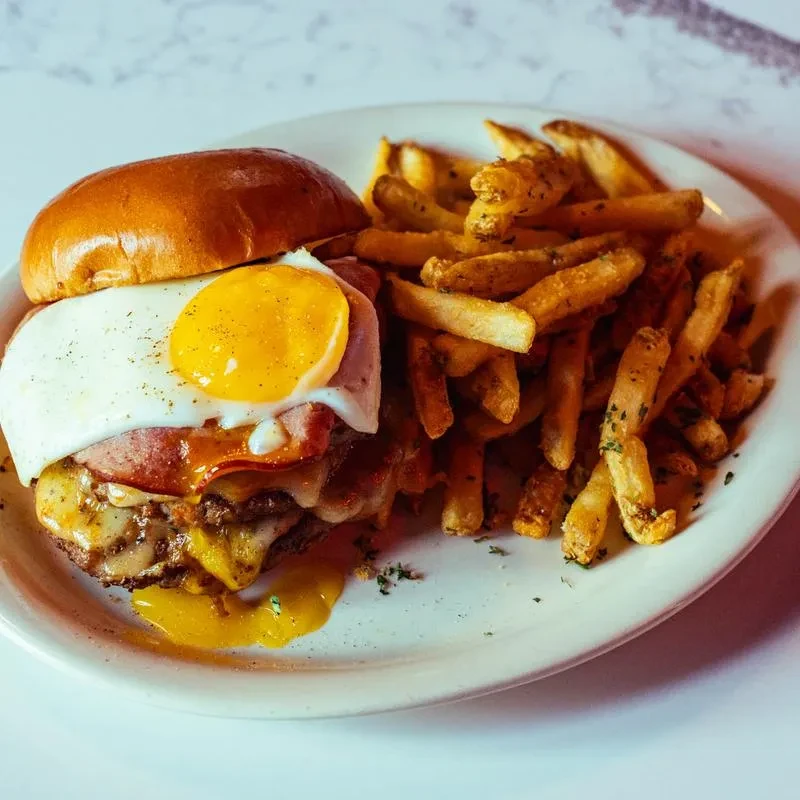 Gourmet burger with runny egg, bacon, melted cheese, and seasoned fries.