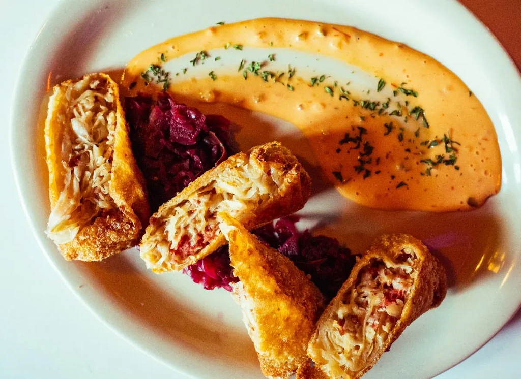 Fried golden rolls, chopped red vegetable, and orange sauce with green herbs.